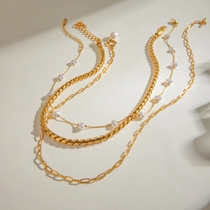 Dettaglio di collane d'oro a strati con perla, catena a graffetta e design a corda