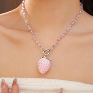 Close-up of a pink strawberry pendant necklace with a polished silver-tone chain on model