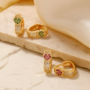 Detail of heart-shaped gold earrings with emerald and ruby zircon inlay on marble