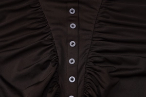Detalle de los botones blancos y la textura plisada en un vestido marrón oscuro