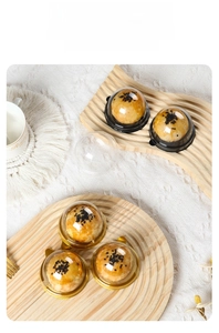 Close-up of clear dome pastry boxes for mooncakes on a rustic wooden tray with dry flowers