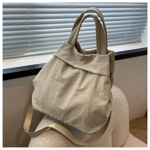 Detailed view of cream nylon tote bag with thick handles on a plush sofa in sunlight