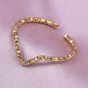 Macro detail of wave-shaped gold ring with hammered texture on purple silk fabric