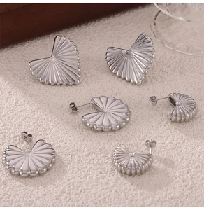Detail of silver pleated fan and heart earrings with geometric crystal studs on beige texture