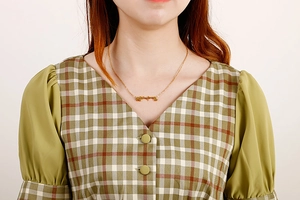 Nahaufnahme einer eleganten goldenen Edelstahlkette mit Buchstaben-Anhänger am Model
