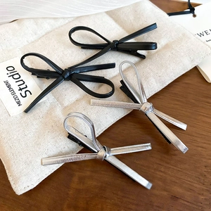 Detail of Y2K faux leather and metallic bow hair clips on a textured rustic fabric
