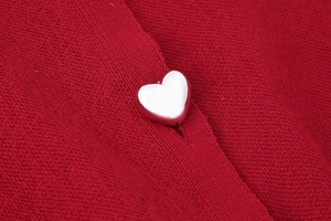 Detailed close-up of silver heart-shaped button on a red long sleeve knit cardigan