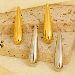 Polished gold and silver teardrop earrings displayed on a textured stone surface