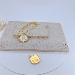 Macro detail of gold plated necklace with a square zircon pendant on a beige stone surface