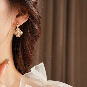 Détail d'une boucle d'oreille fleur dorée avec perles et strass portée par un mannequin