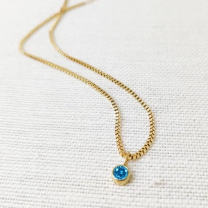 Detail einer goldenen Edelstahlkette mit rundem blauem Geburtsstein-Anhänger