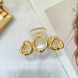 Detail of a transparent acrylic hair claw clip with golden geometric metal accents