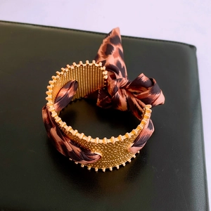 Detailansicht der goldenen Netzmanschette mit elegantem Seidenband im Leopardenmuster