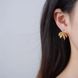 Primo piano di un orecchino a foglia dorata indossato da una modella con luce soffusa