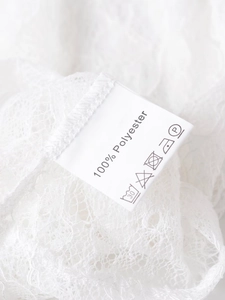 Detail view of white lace fabric texture and 100% polyester material care label