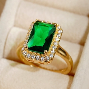 Macro shot of an emerald-cut green gemstone ring with a gold band and diamond halo