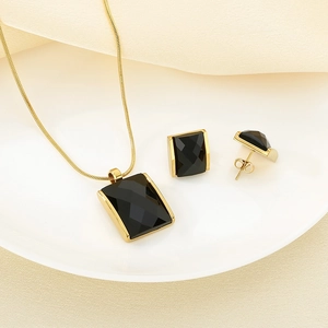 Detail of gold snake chain necklace with rectangular black gemstone pendant and studs