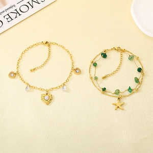 Detail of gold-tone layered anklets featuring heart, starfish charms and green stones