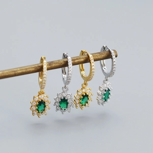 Detailed view of silver and gold hoop earrings with emerald green zircon pendants