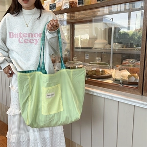 Detail of light green canvas tote bag with plaid handles and brand logo in a bakery