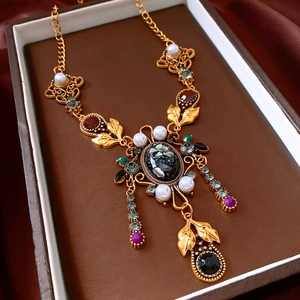 Dettaglio macro di una collana vintage dorata con cristalli colorati e nappe di perle su velluto