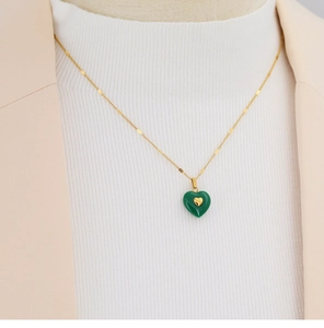 Close-up of a gold necklace featuring a green heart pendant with a small gold heart inlay
