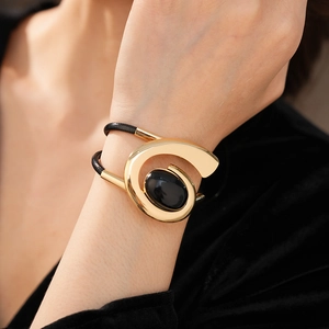 Detail of a vintage oval black gemstone gold bracelet with woven leather strap on wrist