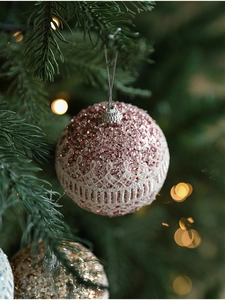 Close-up of pink glitter Christmas ball with white lace mesh on a festive tree branch