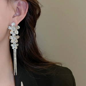 Detail showing silver flower earrings with long metallic tassels on model side view