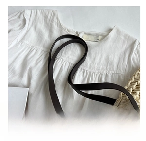 Detail of white pleated texture fabric with black leather shoulder strap on straw tote bag
