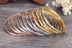 Polished minimalist metal bracelets in gold, silver, and rose gold on a wooden background