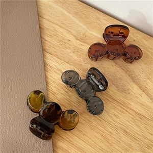 Three minimalist small hair claw clips in brown, grey, and amber on a wooden surface