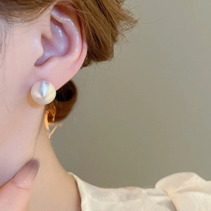 Close-up of matte white pearl stud earring with brushed satin finish on ear