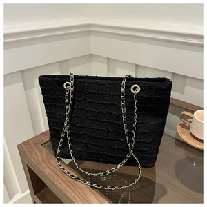 Detail of black tote bag with quilted texture and gold chain strap on wooden surface