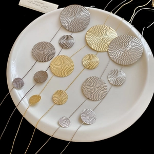 Detail of layered gold and silver textured disc pendants on a ceramic tray