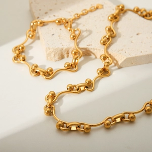 Golden horseshoe link chain necklace with polished beads on a minimalist stone background