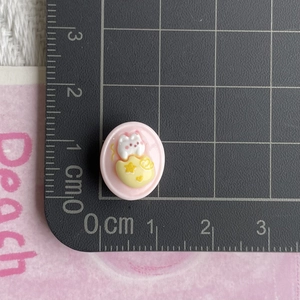 Pink resin kitten charm size measurement on a grid mat for DIY jewelry making crafts