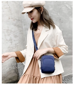 Close-up of blue nylon crossbody phone bag with gold zippers worn over a beige suit