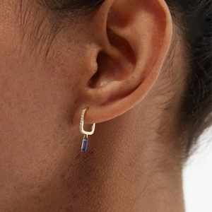 Close-up of gold sapphire drop earrings with zircon accents worn by a model