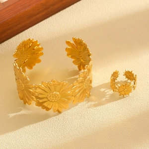Macro detail of gold sunflower cuff bracelet and matching ring on a textured beige surface