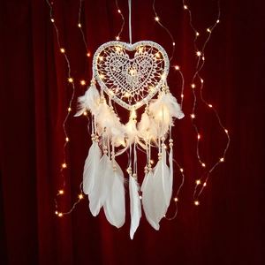 White lace heart dream catcher with feathers and warm LED lights on red background