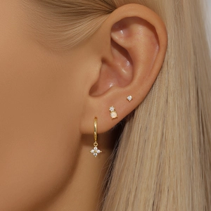 Macro shot of gold earrings set featuring bow design and opal stones on a model ear