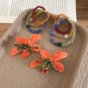 Close-up of handmade orange floral earrings with colorful beads on a vintage tray