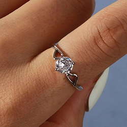 Close-up of silver open ring featuring a sparkling central gem and hollow heart designs