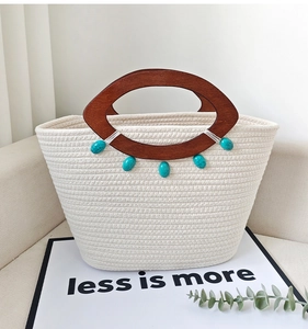 Detail of beige woven tote bag with wooden handles and turquoise beads on a sofa