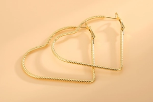 Detail shot of large golden heart-shaped hoop earrings with textured twisted metal design