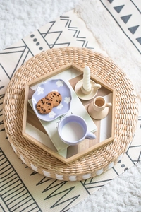 Detail showing a purple petal saucer with a ceramic mug on a natural woven pouf