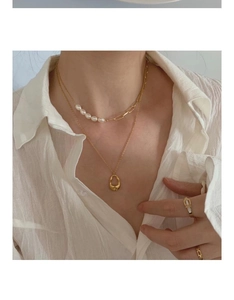 Detail of layered gold necklaces with pearls and drop pendant on a white shirt