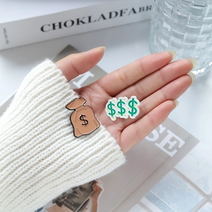 Golden money bag and dollar sign enamel lapel pin set held in hand for display