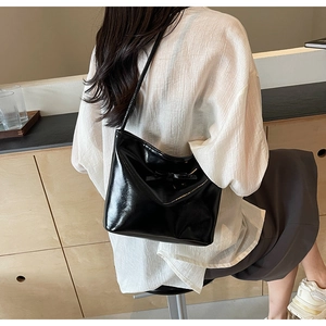 Side view of a black patent leather tote bag with a chic bow and glossy mirror finish
